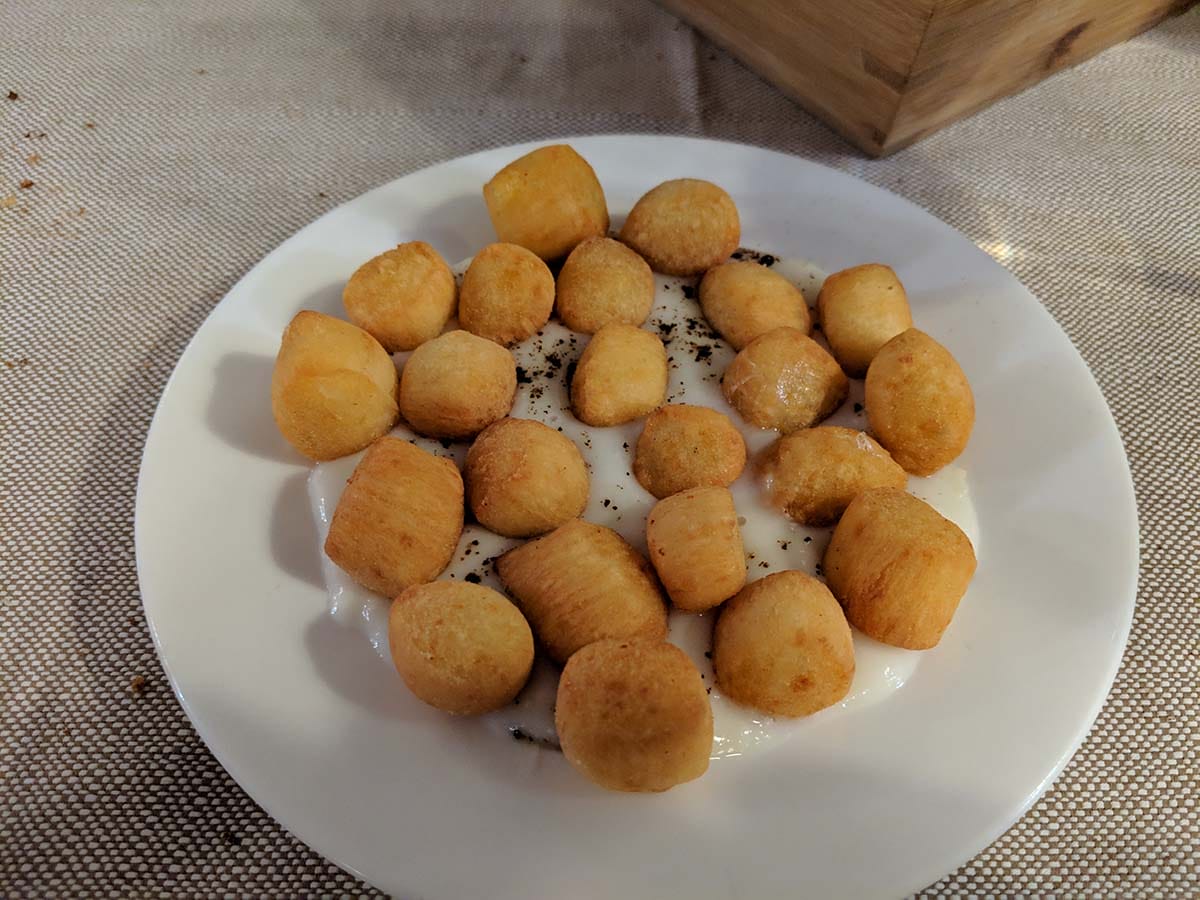 white plate of deep fried gnocchi on top of a creamy white sauce.