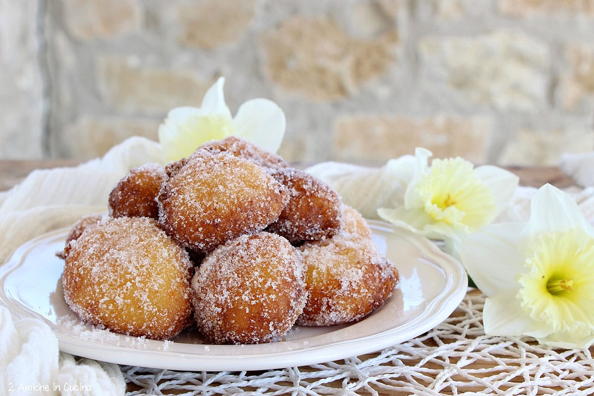 white plate of small donut hole-like pastries with white flowers nearby.