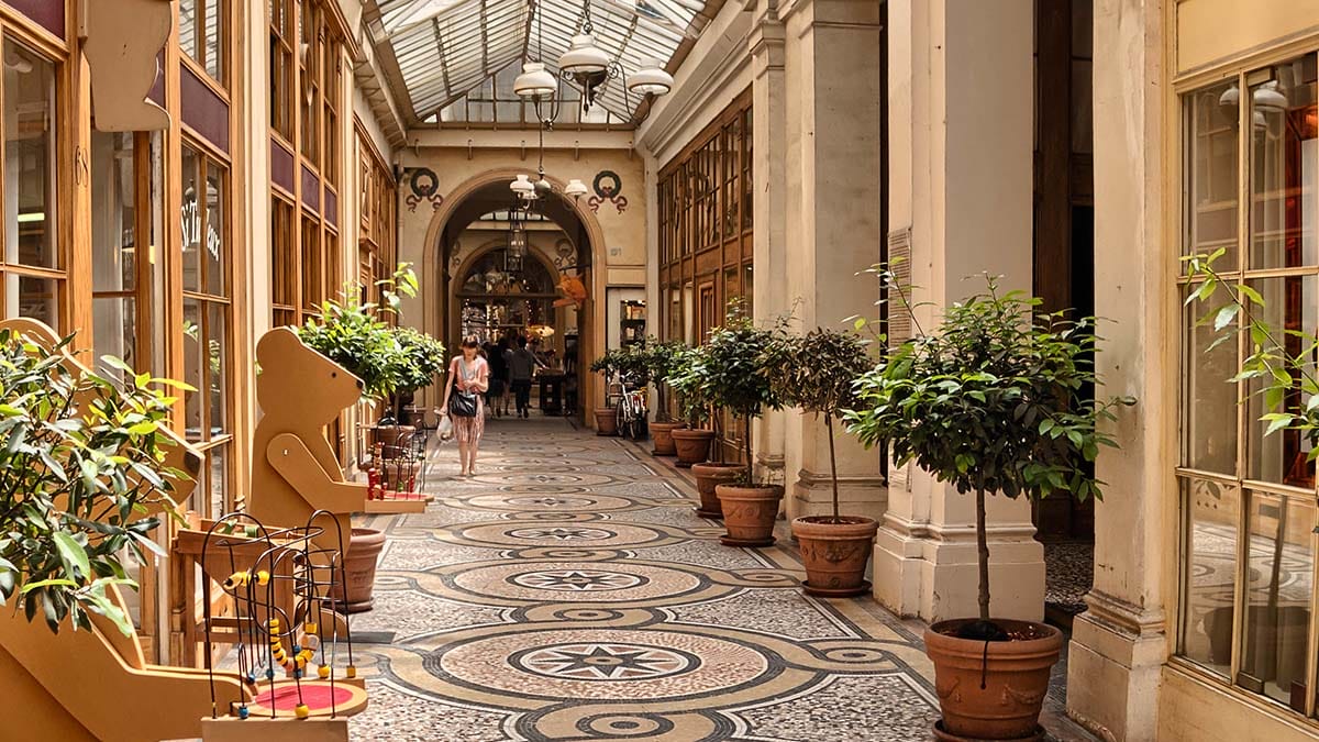 Paris passageway with a glass ceiling, mosaic floors, and potted plants.