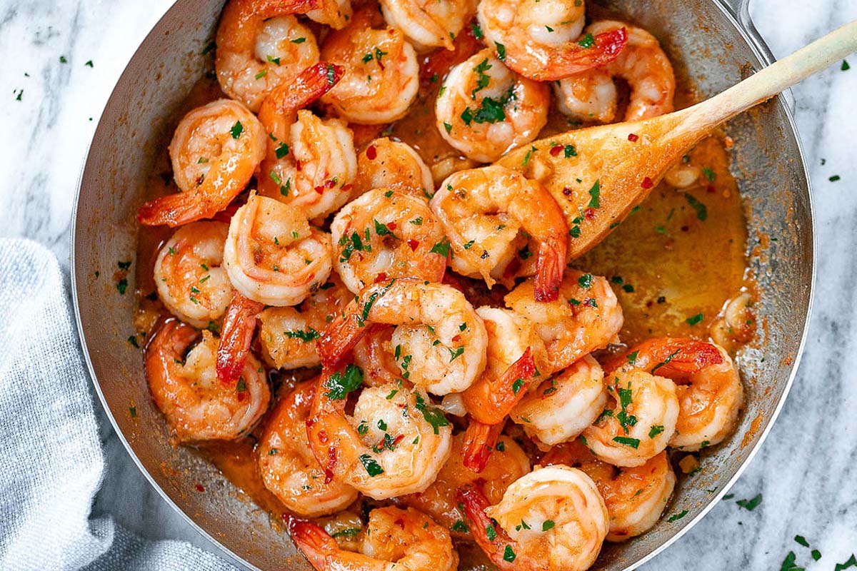 large pot of cooked shrimp with sauce and herbs.