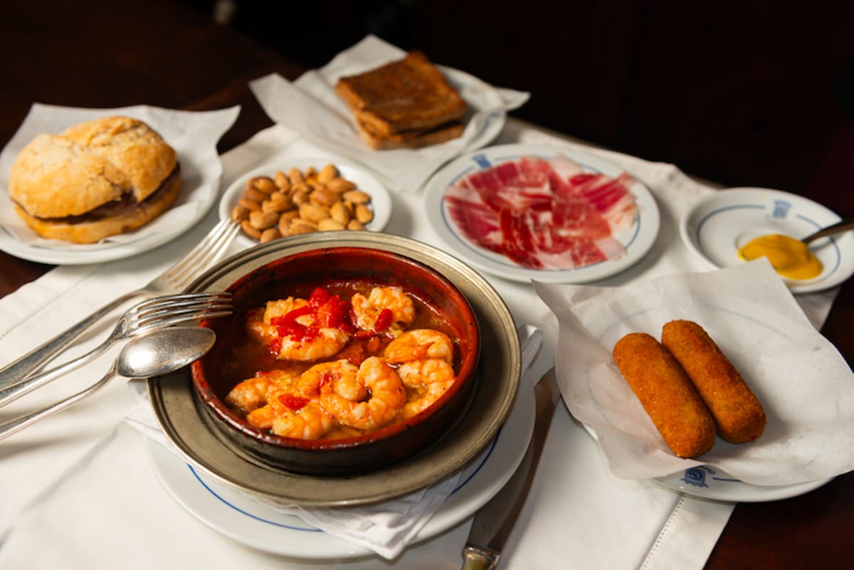dish of shrimp, croquettes, ham, and other Portuguese dishes on a white-covered table.