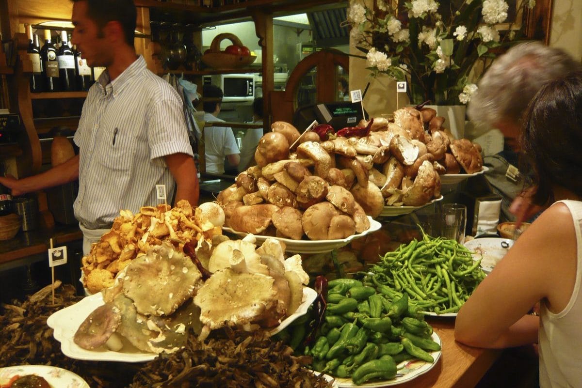 platters of beans, peppers, and mushrooms on a wooden bar in a dimly lit restaurant.