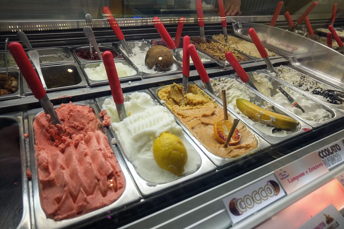 stainless steel food containers filled with different flavors of gelato with a scoop in each one.