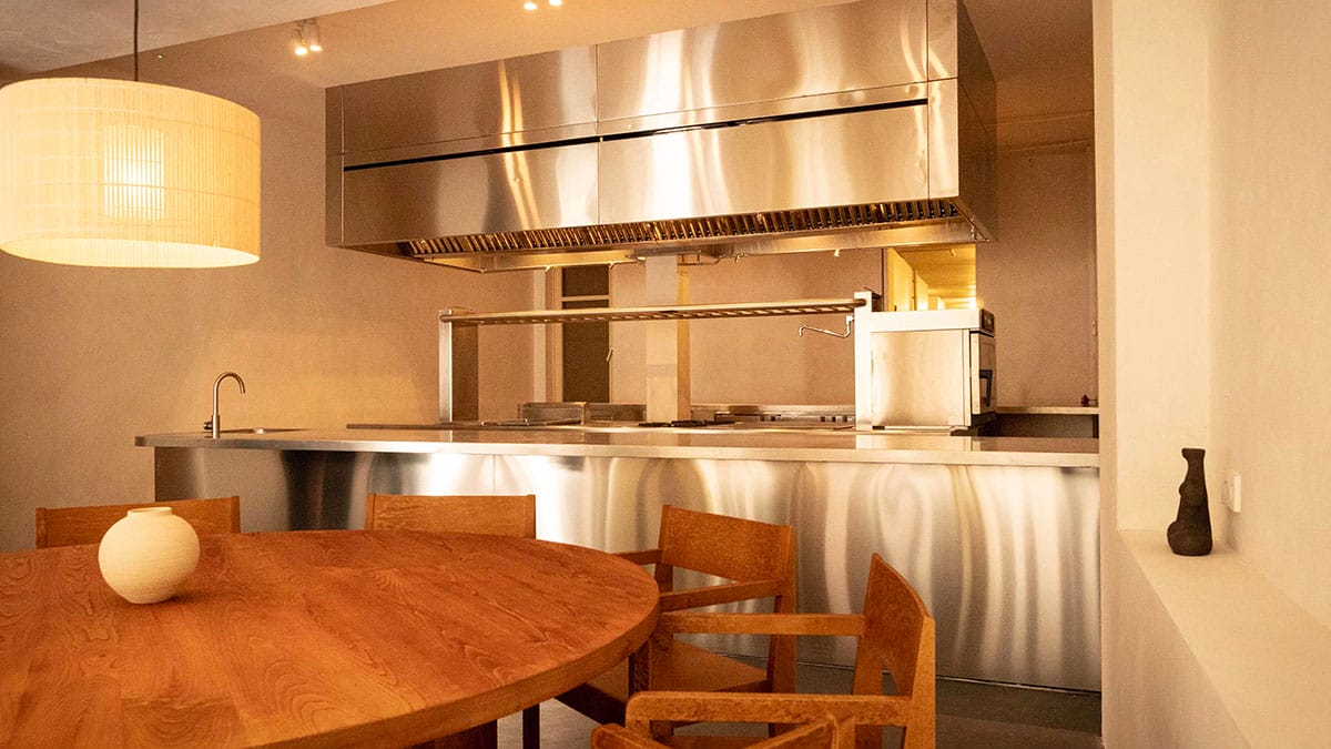 wooden table and chairs near a stainless steel kitchen.