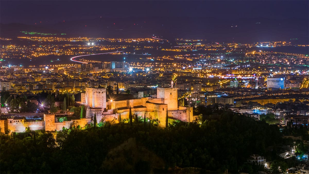nighttime vista of the Alhambra and the Granada skyline as viewed from a hill above.