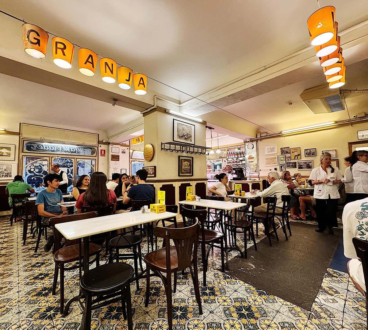 tables and chairs in a restaurant with "granja" spelled out on hanging lanterns from the ceiling.