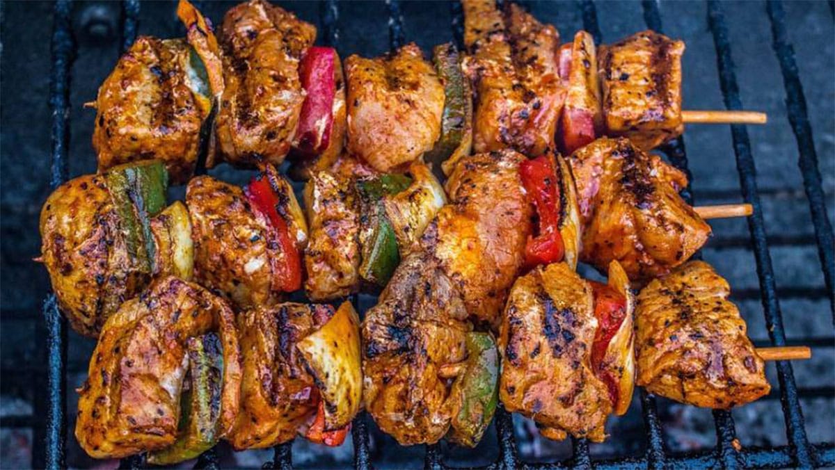 three kebabs of meat and veggies on a grill.