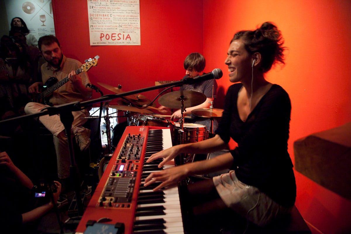 guitarist, dummer, and keyboardist singing and playing on a small stage.