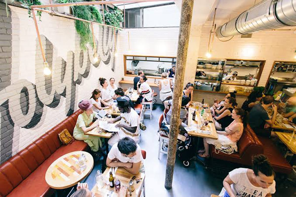 groups of people sitting at wooden tables in a sunlit restaurant.