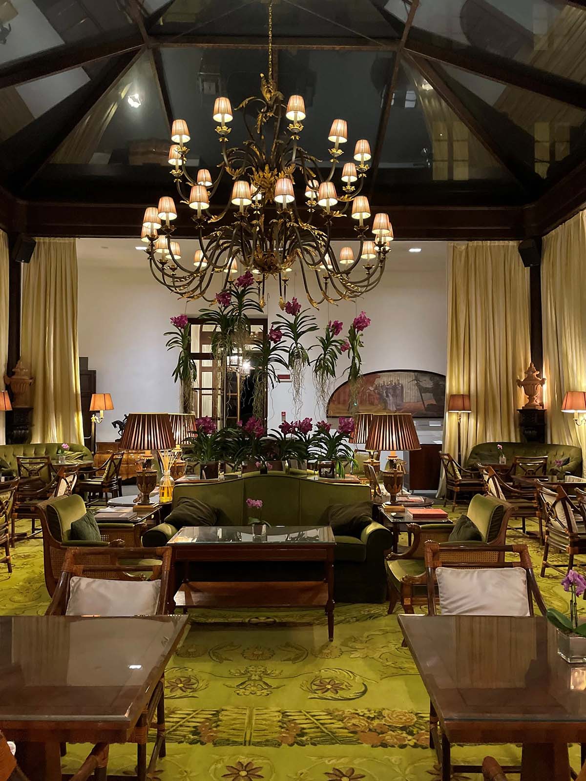 tables and couches in a high-ceilinged room with a chandelier.