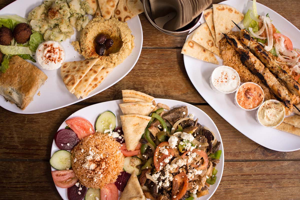 dishes of rice, pita bread, skewers, and veggies on white platters.