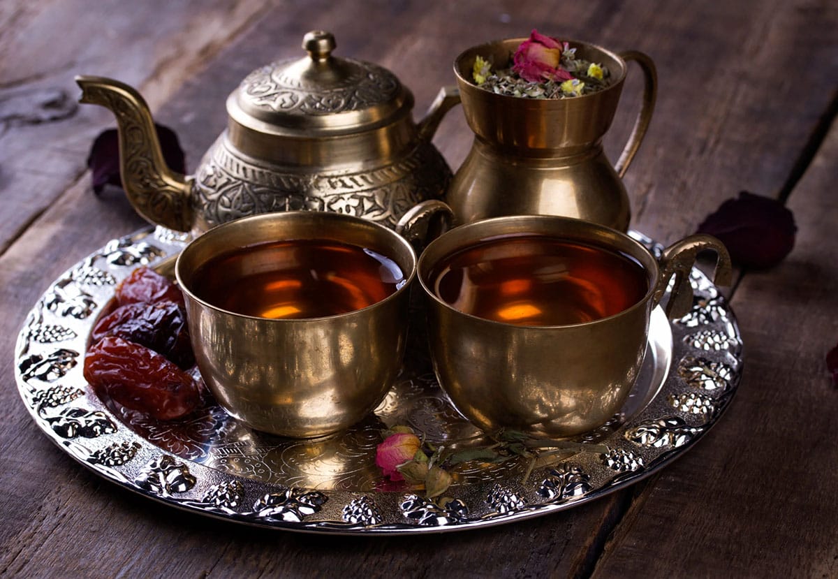 two cups of hot tea with a metal teapot on a tray.