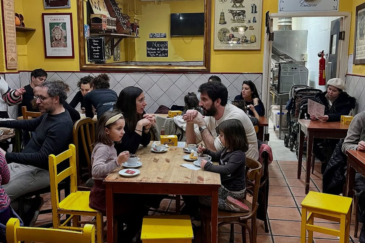 families sitting at tables while drinking hot chocolate and eating churros.