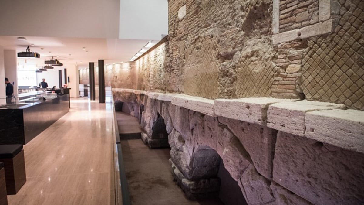 arched walls of an aquaduct along the wall of a brightly lit basement with a coffee shop nearby.
