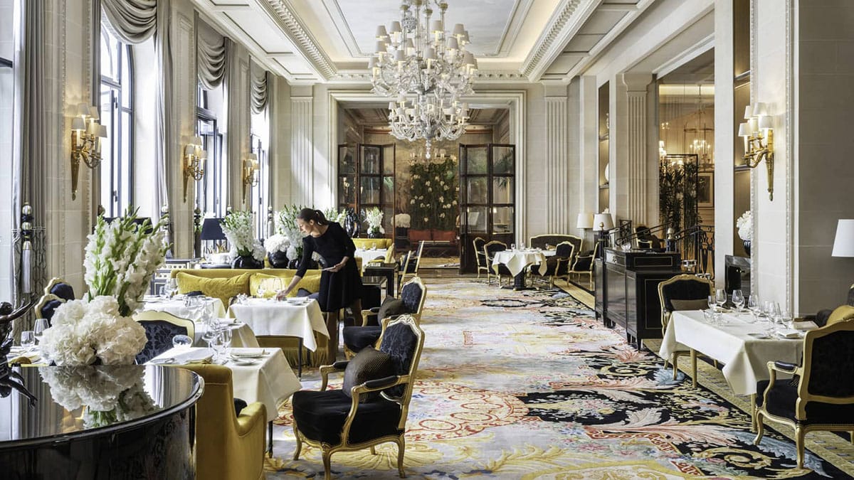 woman setting tables in a sunlit hotel dining room.