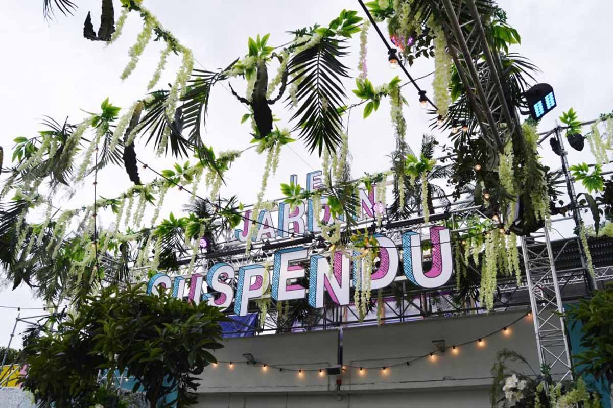 large sign reading "Le Jardin Suspendu" with plants hanging from wires and scaffolding.