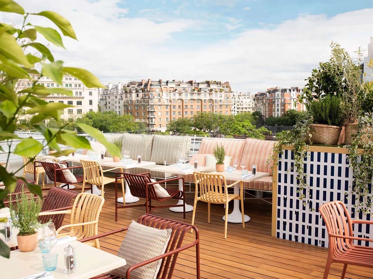 tables and chars on a rooftop bar with potted plants.
