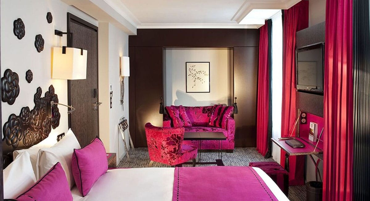 hotel room with a bed, sofa, chair, and windows with pink curtains.