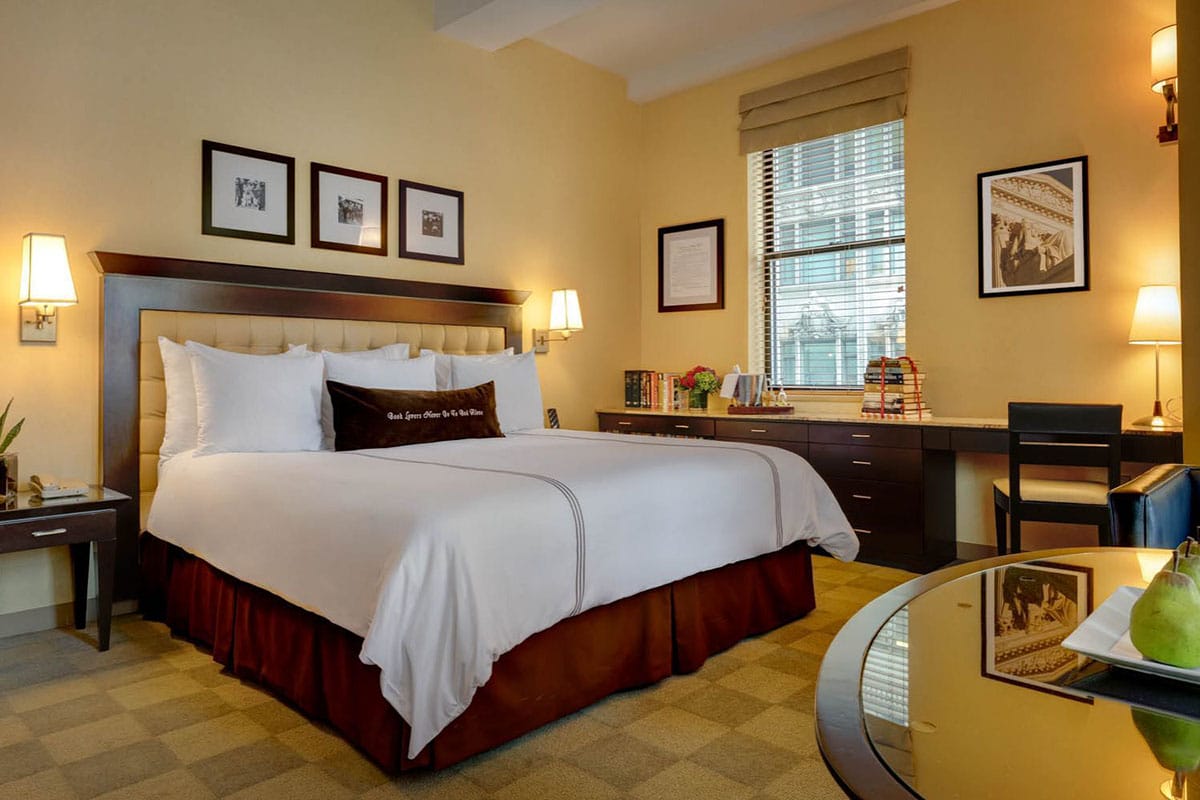 large bed in a warmly lit bedroom with a desk and books nearby.