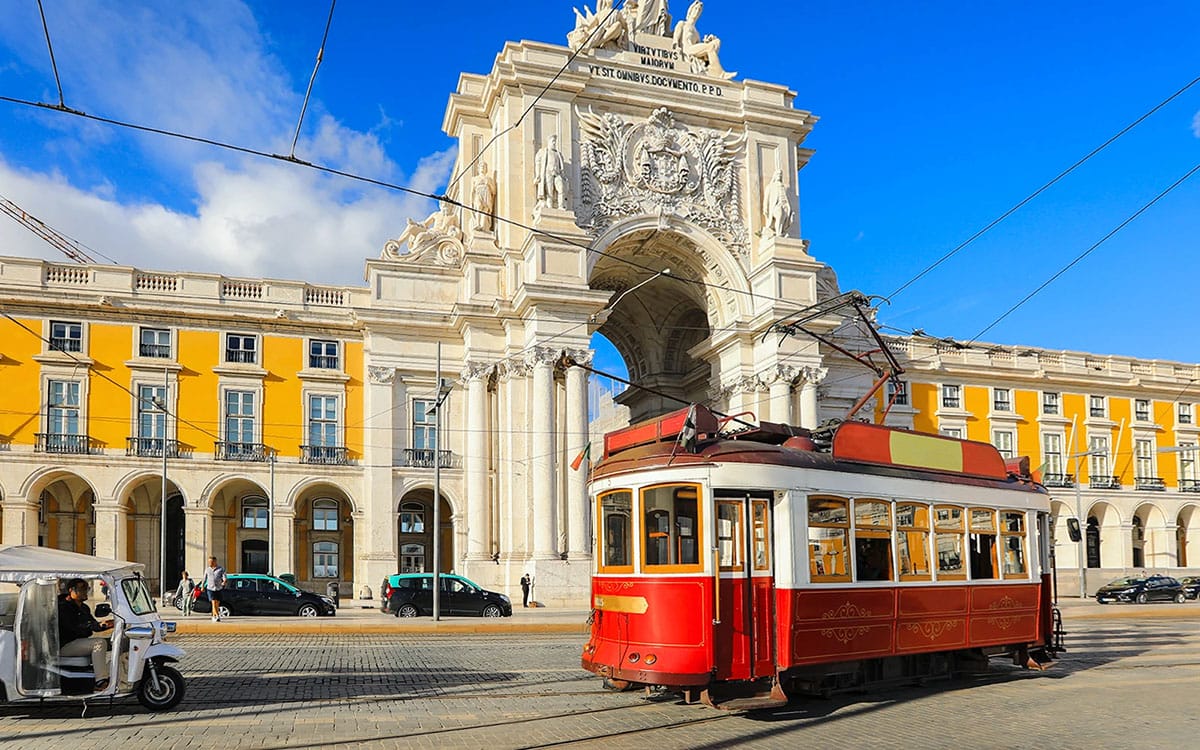 red tram in front of a large ornate archway and historic building.