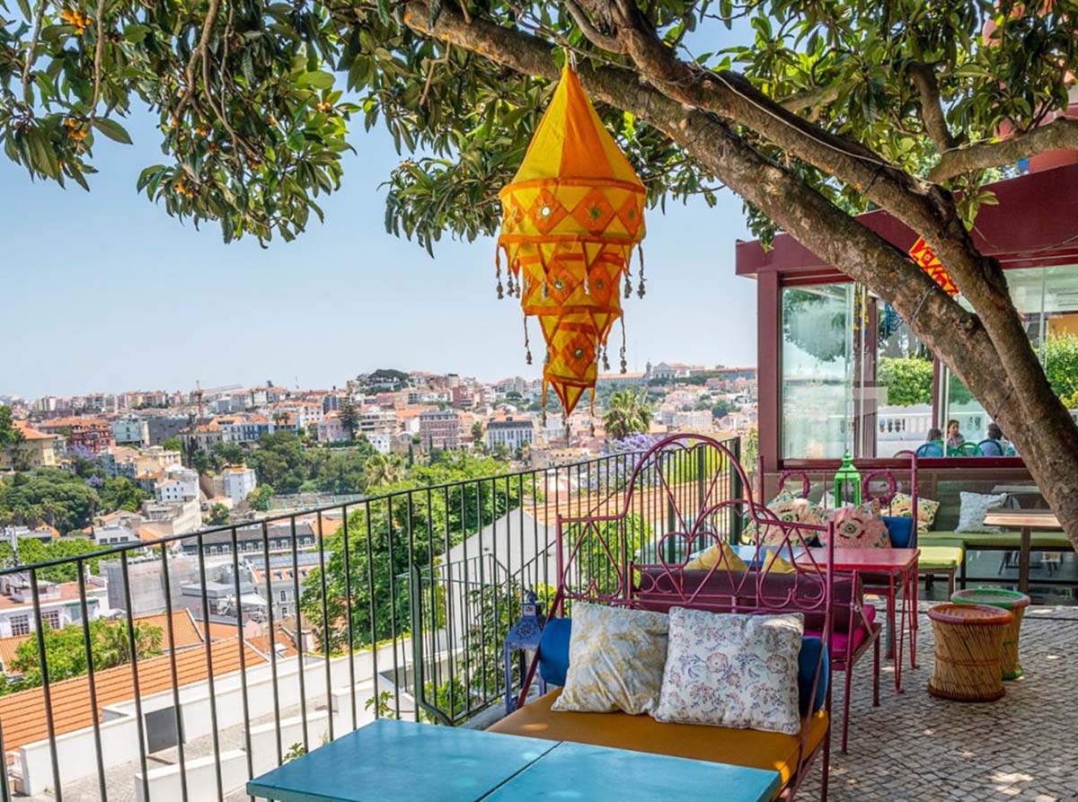 large tree shading tables and chairs on a brick terrace overlooking Lisbon.