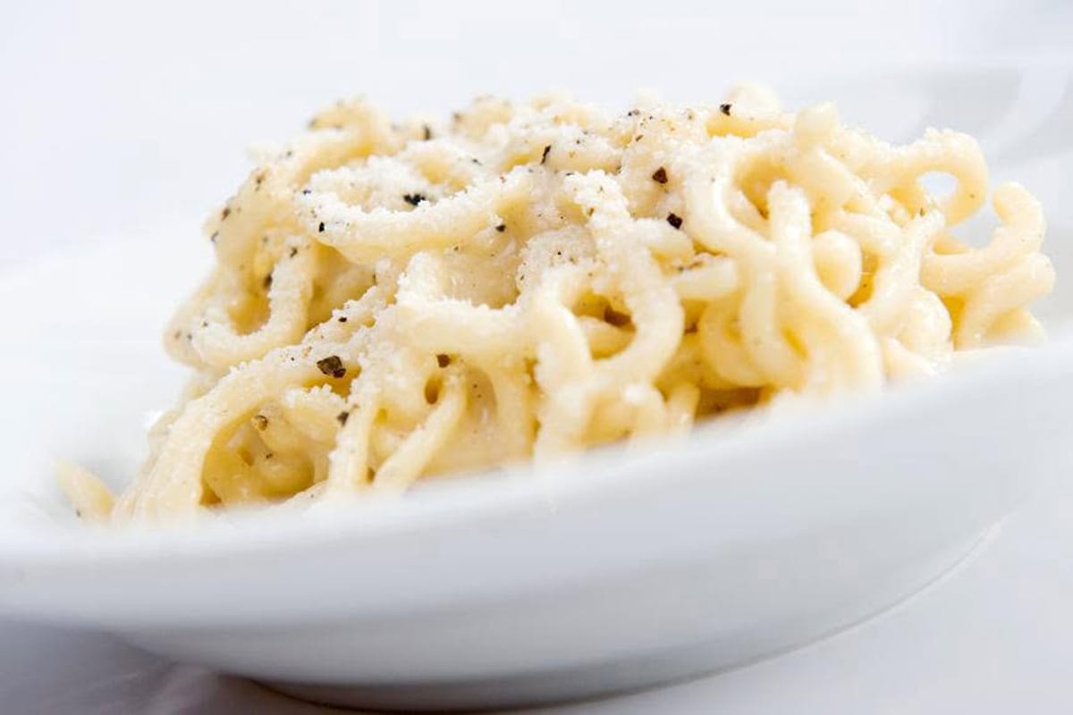 white dish of cacio e pepe topped with grated cheese and black pepper.