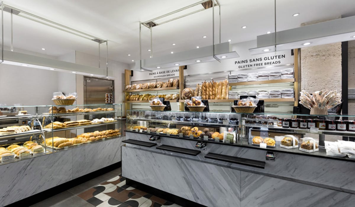glass shelves of baked goods and breads in a marble-lined bakery.