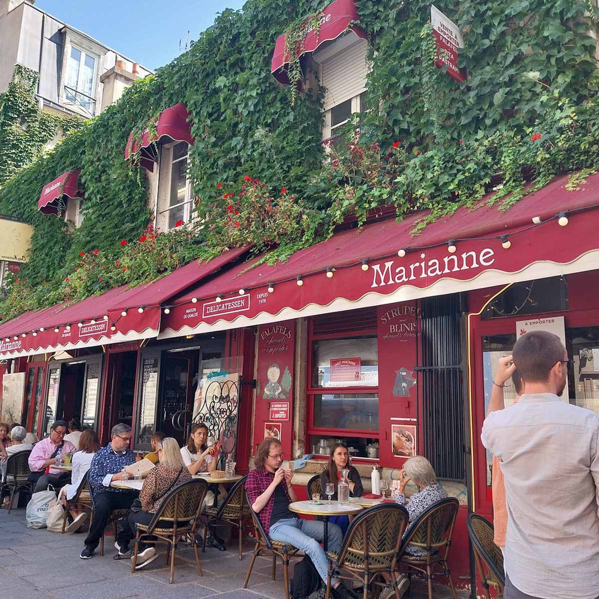 people sitting at tables outdoors under a red awning.