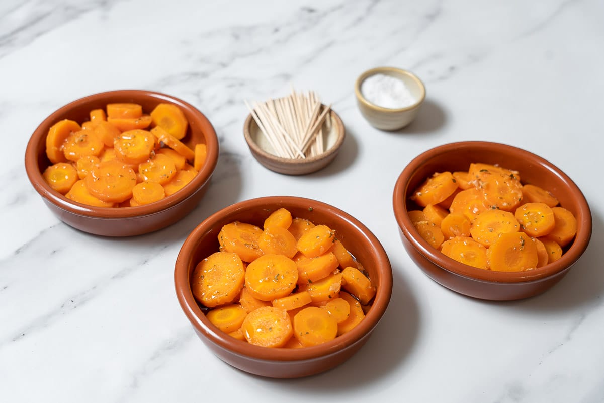 three clay dishes filled with sliced marinated carrots.