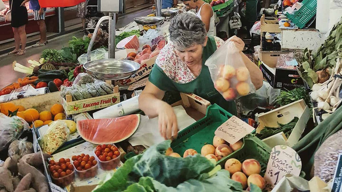 vendor bagging produce for a client at a Lisbon food market.