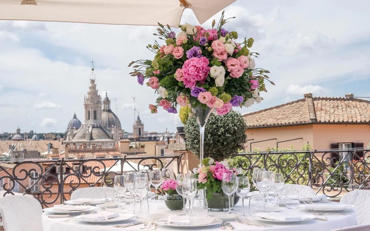 large white-covered round table on a rooftop with a large pink floral arrangement in the center.