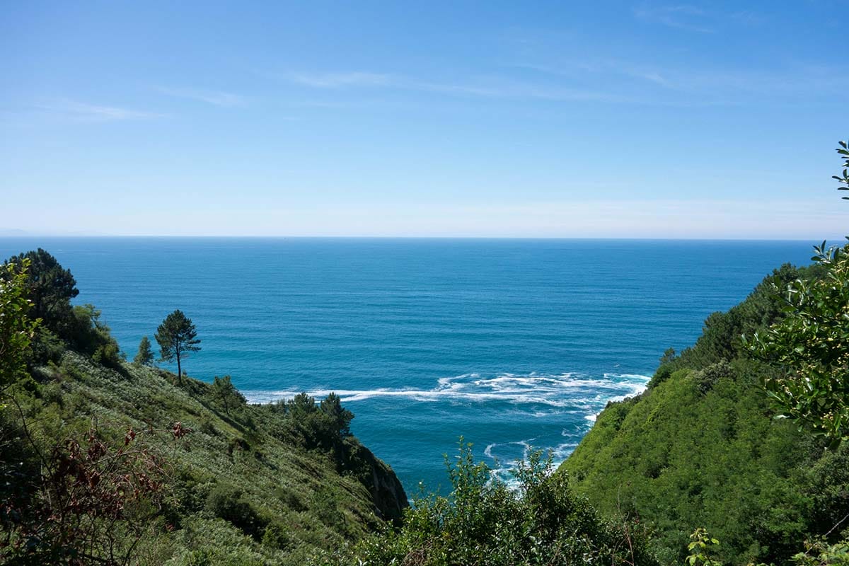 view of the ocean from steep, tree-lined mountains.