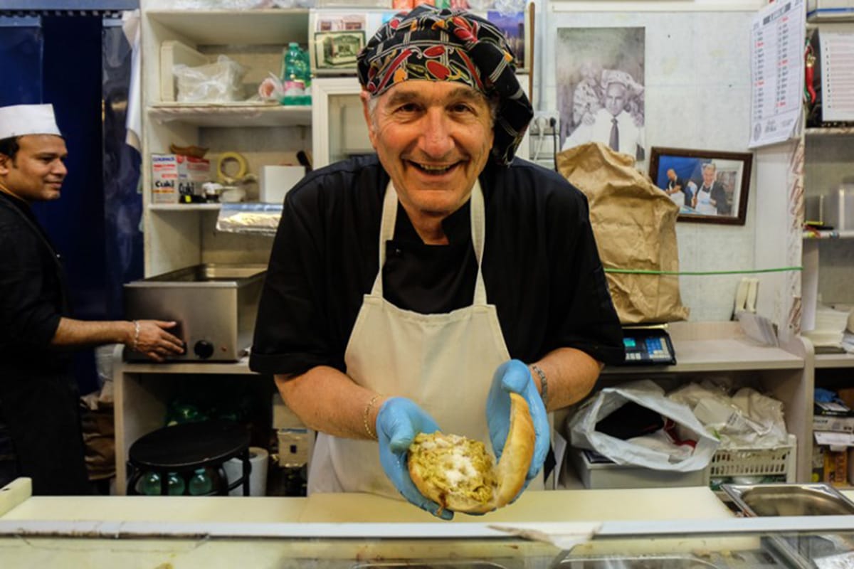 man assembling a large sandwich in a restaurant kitchen.