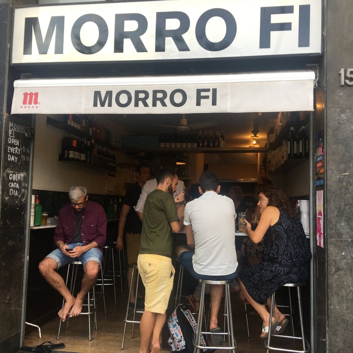 people standing and sitting at small tables in a small bar.