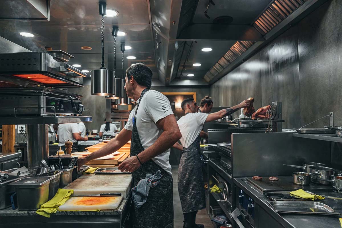 men wearing aprons cooking in a stainless steel commercial kitchen.