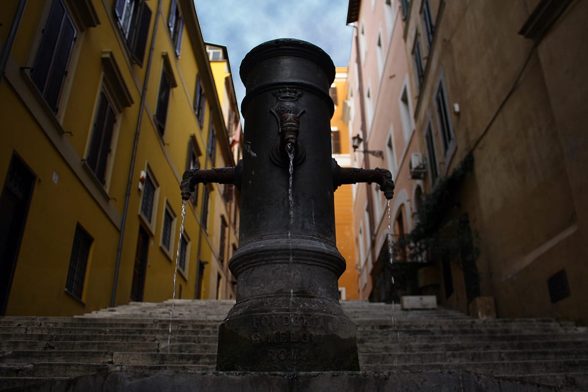 cold flowing water from a public fountain on a staircase in a Roman street.