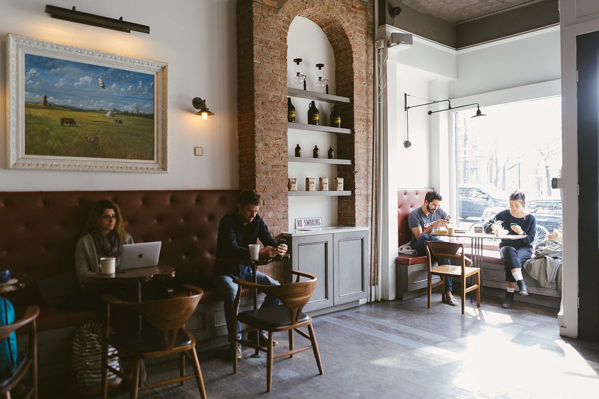 people sitting at small tables and chairs in a white-walled coffee shop overlooking the street.