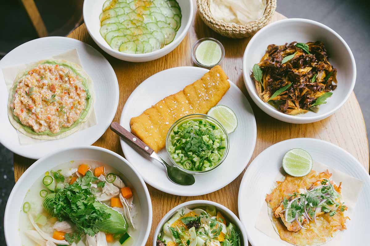 plates of Mexican salads, tortillas, and toppings on white plates on a round wooden table.