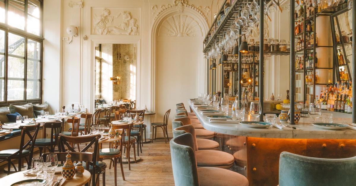 tables and chairs with a marble-topped bar in a sunlit restaurant.