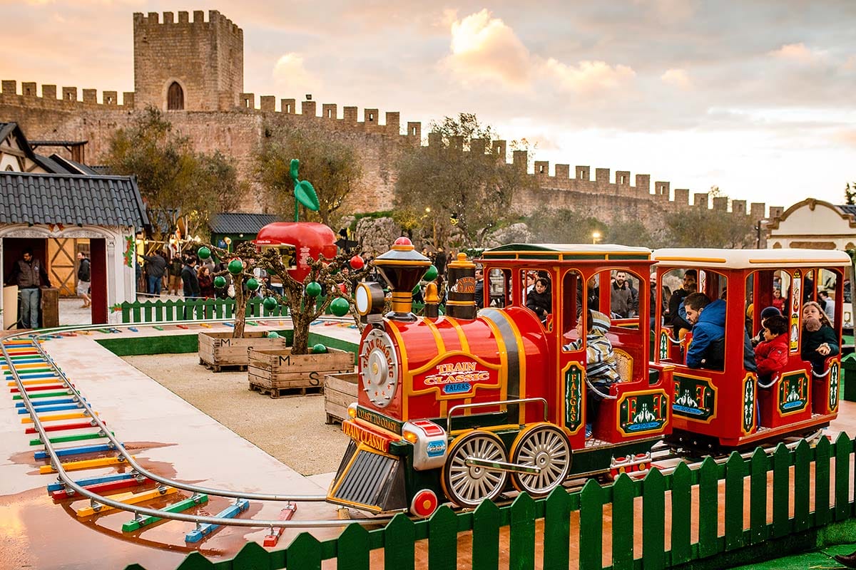 children riding a train at Obidos Vila Natal near a castle.