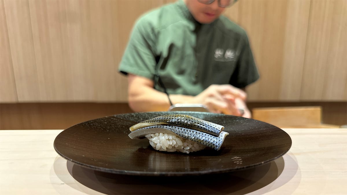 sushi chef behind the counter with a plate of sushi in front.