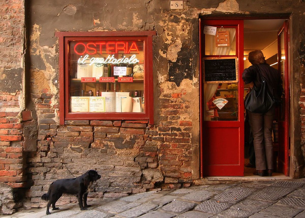 man entering a red doorway into a restaurant with a black dog on a leash waiting outside.