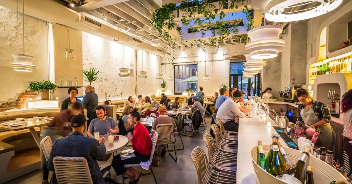 white stucco-walled restaurant with a high ceiling and skylights and many tables, chairs, and a bar.
