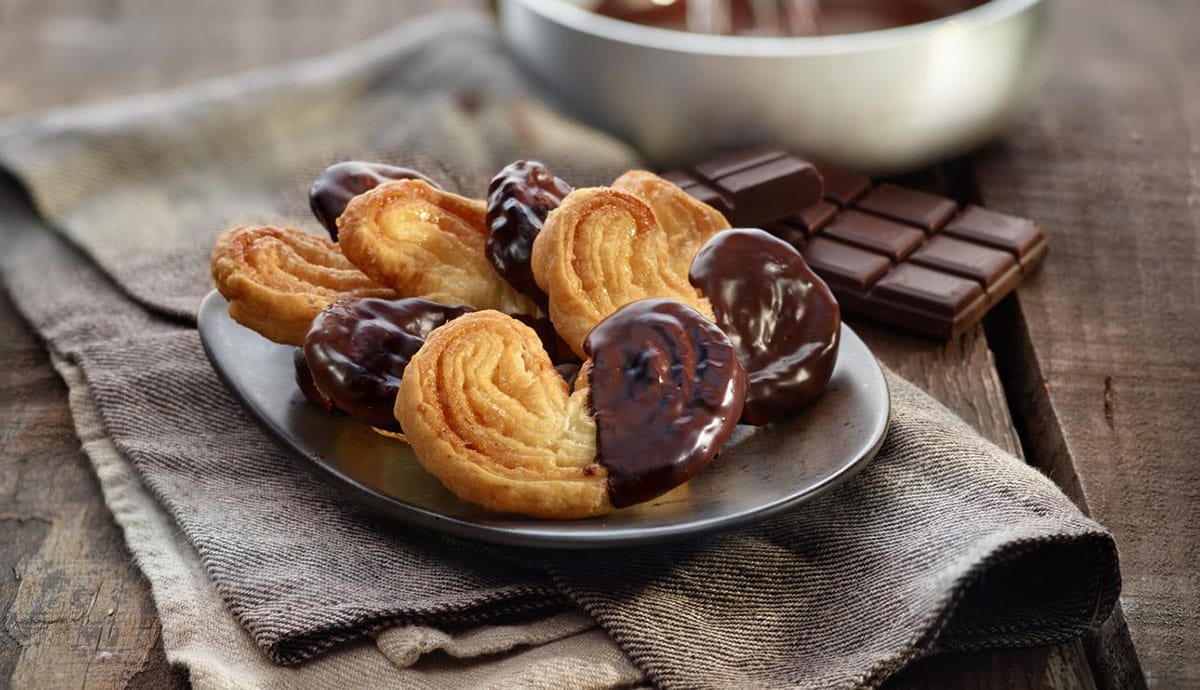 shiny plate of chocolate-dipped palmiers on top of a cloth napkin.