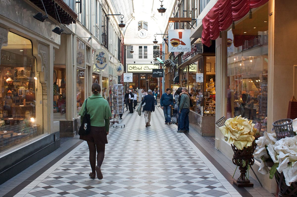 woman walking down a glass ceilinged passageway lined with shops.