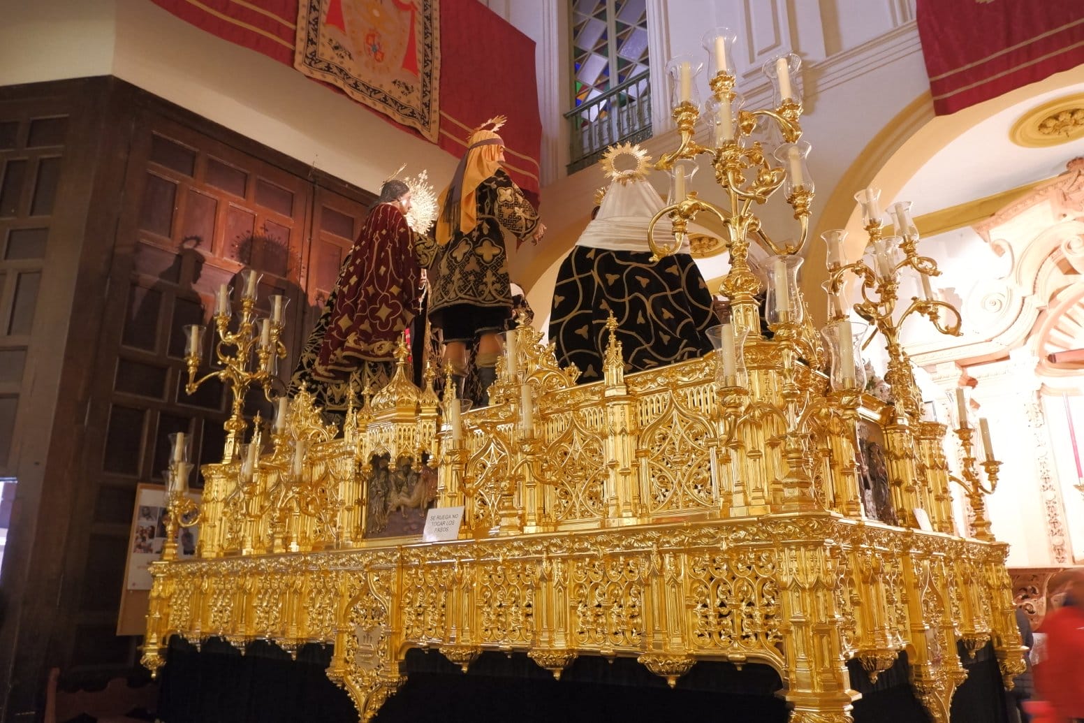 large ornate gold float with three sculptures on top in a Seville church.
