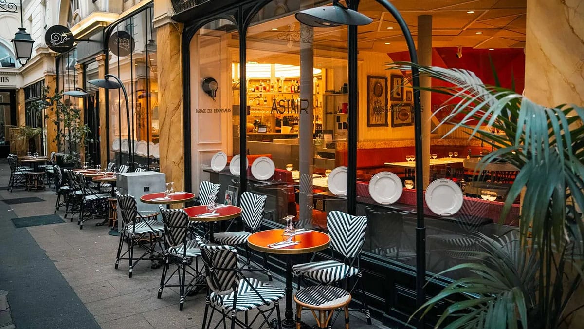 striped chairs at cafe tables outside of a restaurant in one of Paris' covered passageways.