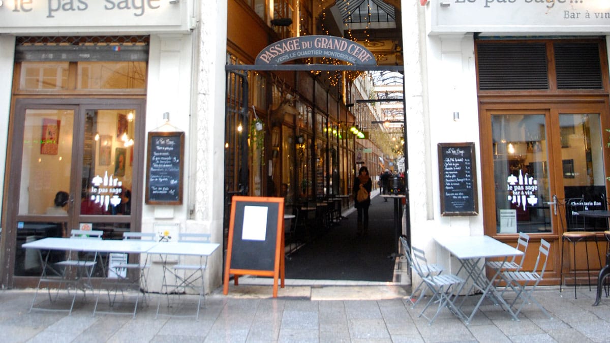 entrance to Passage du Grand Cerf in Paris with cafe tables and chairs on either side.