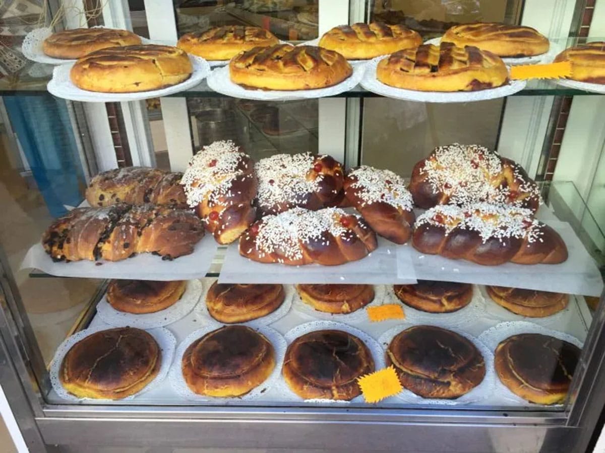 three shelves of baked pastries and braided breads at an Italian bakery.