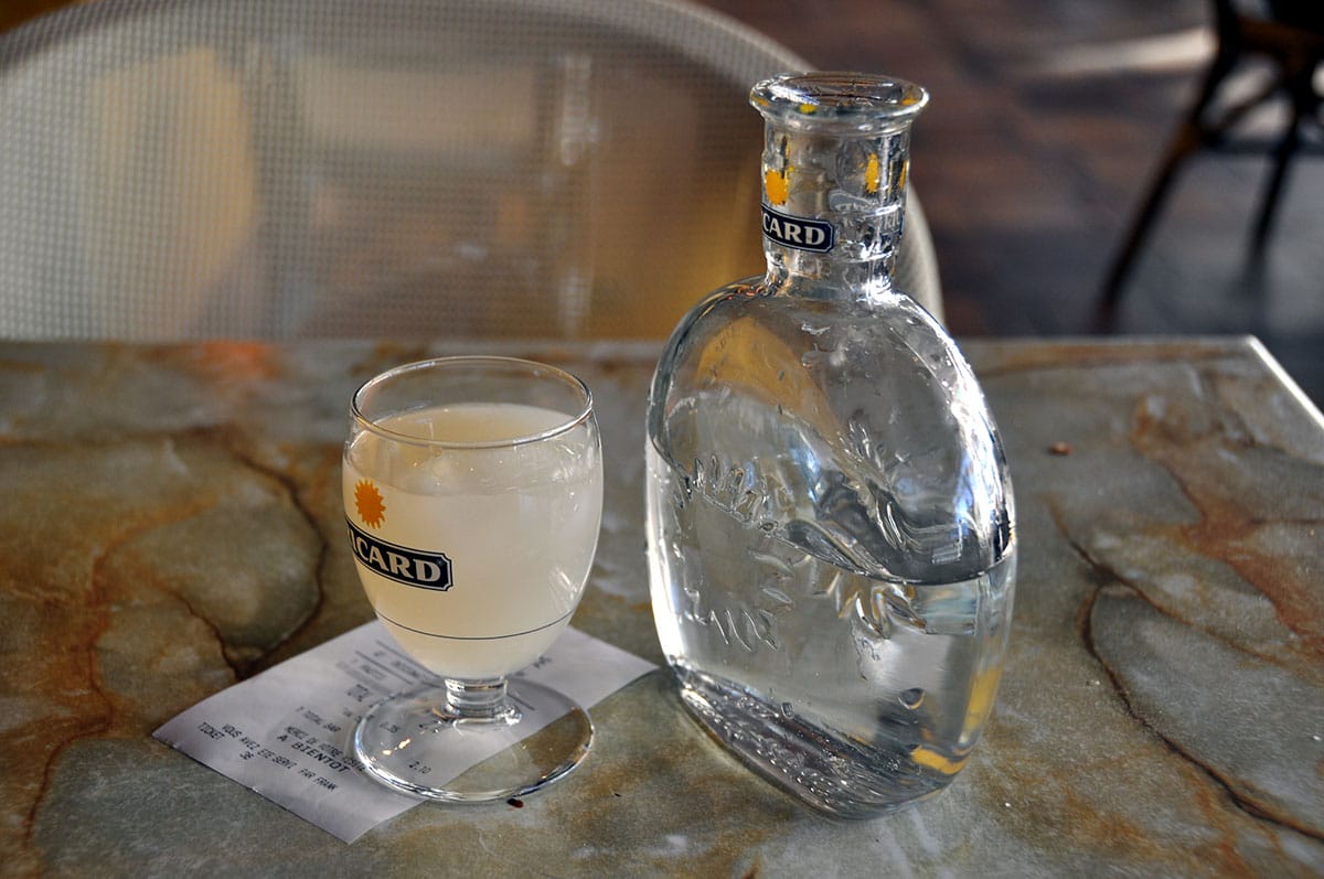 glass bottle of pastis with a small glass of it on a marble table.